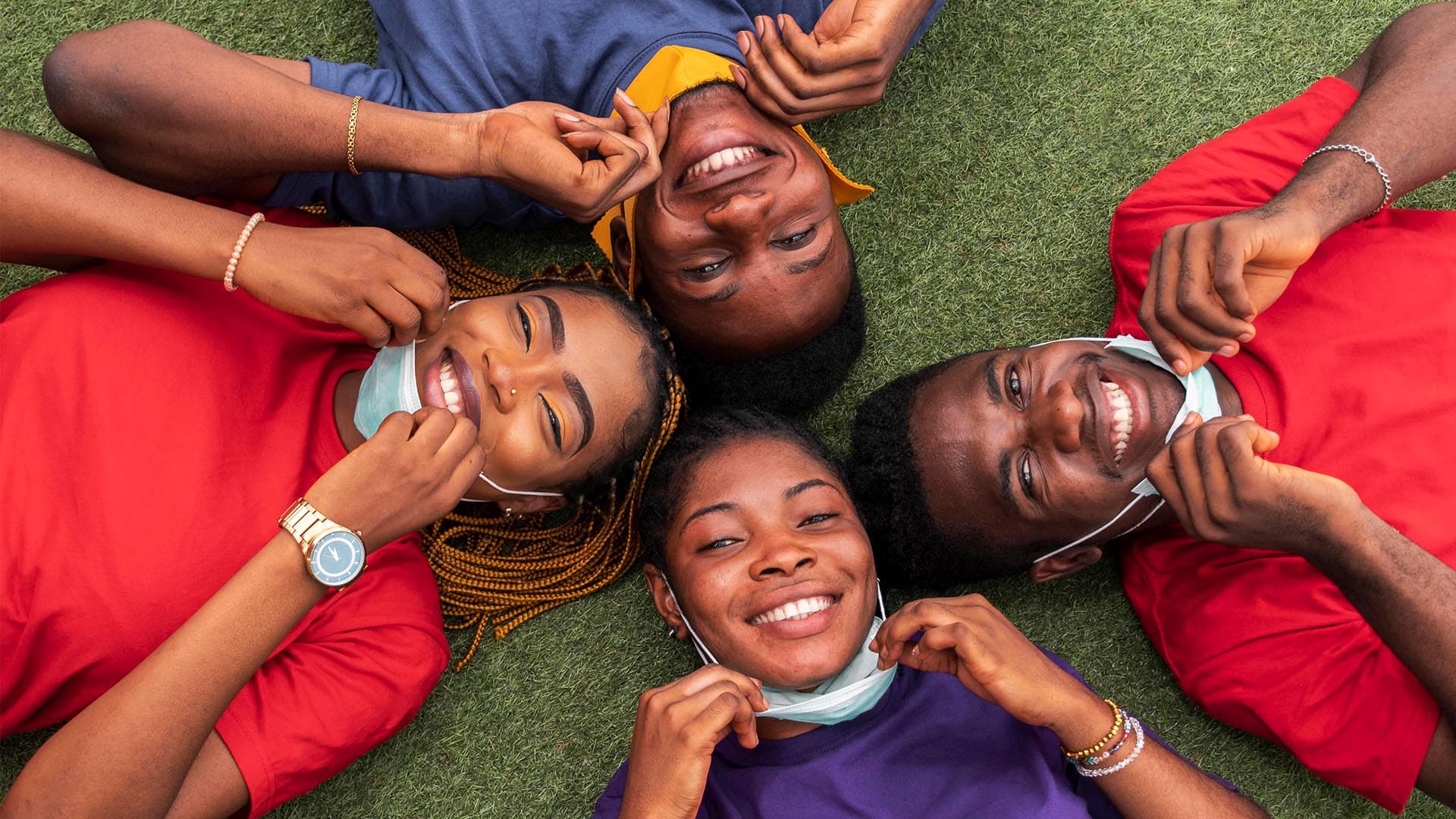 Friends lying on the grass with their heads together, smiling